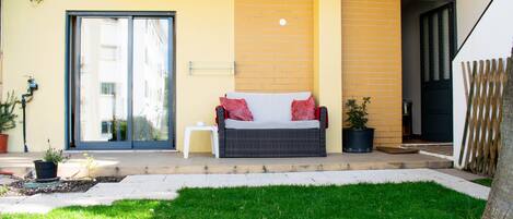A patio with a wicker sofa, a small table, and a potted plant.