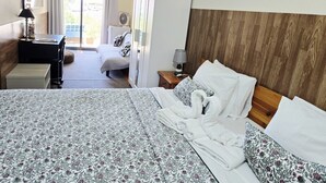 A hotel room with a bed, a desk, a chair, a bedside table with a lamp, a wall-mounted fan, and a view of the outdoors through a window. - Dream Lagos B&B (Lagos)