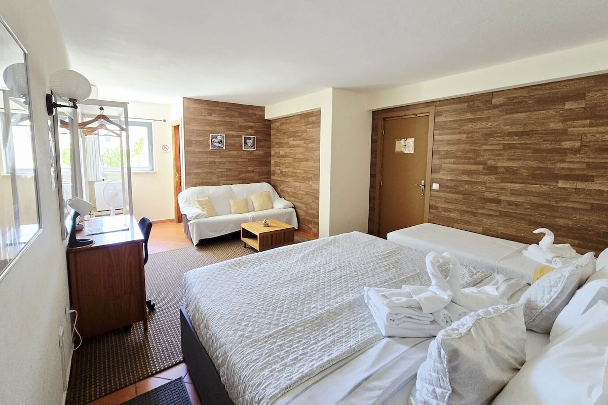 A hotel room with a bed, a desk, a chair, a sofa, and a wardrobe.