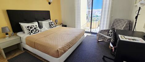 A hotel room with a bed, a desk, a chair, a balcony with a view, and an air conditioning unit.