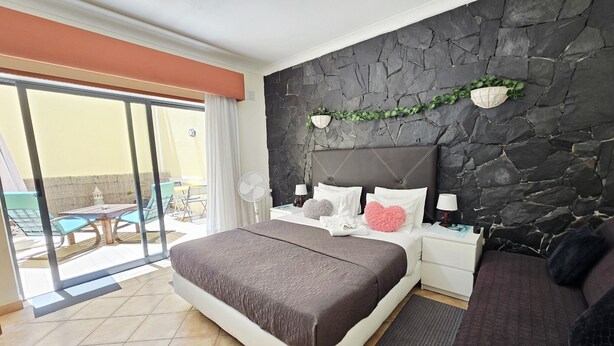 A bedroom with a large bed, a stone wall, a balcony with a table and chairs, and a view of the outdoors. - Dream Lagos B&B (Lagos)