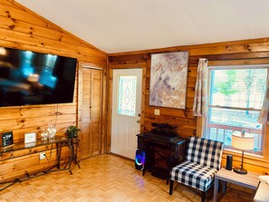 A room with wooden walls, a television, a desk, a chair, and a window with blinds. - 3 bdrm 2 BA cabin with WiFi, AC near Surry, Hopewell, Wakefield& Prince George (Spring Grove)