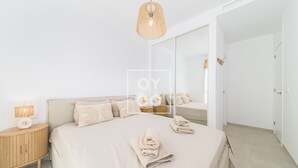 Un dormitorio moderno con una cama grande, mesitas de noche, una lámpara colgante y un espejo que refleja la habitación.