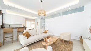 Una sala moderna con sofá, mesa de centro y sillas, una zona de cocina con taburetes de bar y una mesa de comedor.