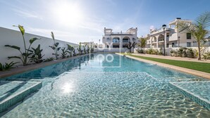 Una piscina con agua cristalina, rodeada por un edificio blanco con varios balcones y un césped bien cuidado.
