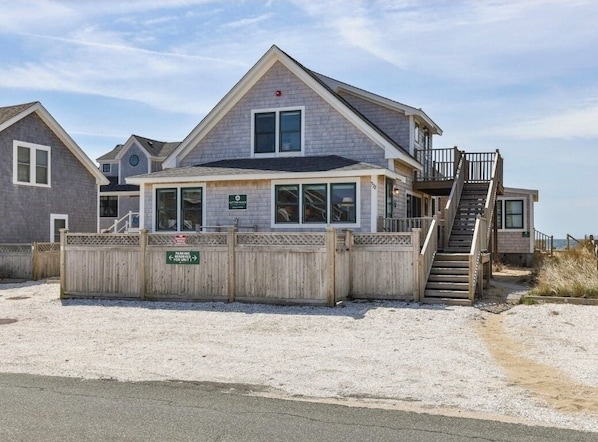Une maison de plage dotée d’un balcon, d’un escalier menant à l’étage supérieur et d’un panneau indiquant la disponibilité des places de stationnement.