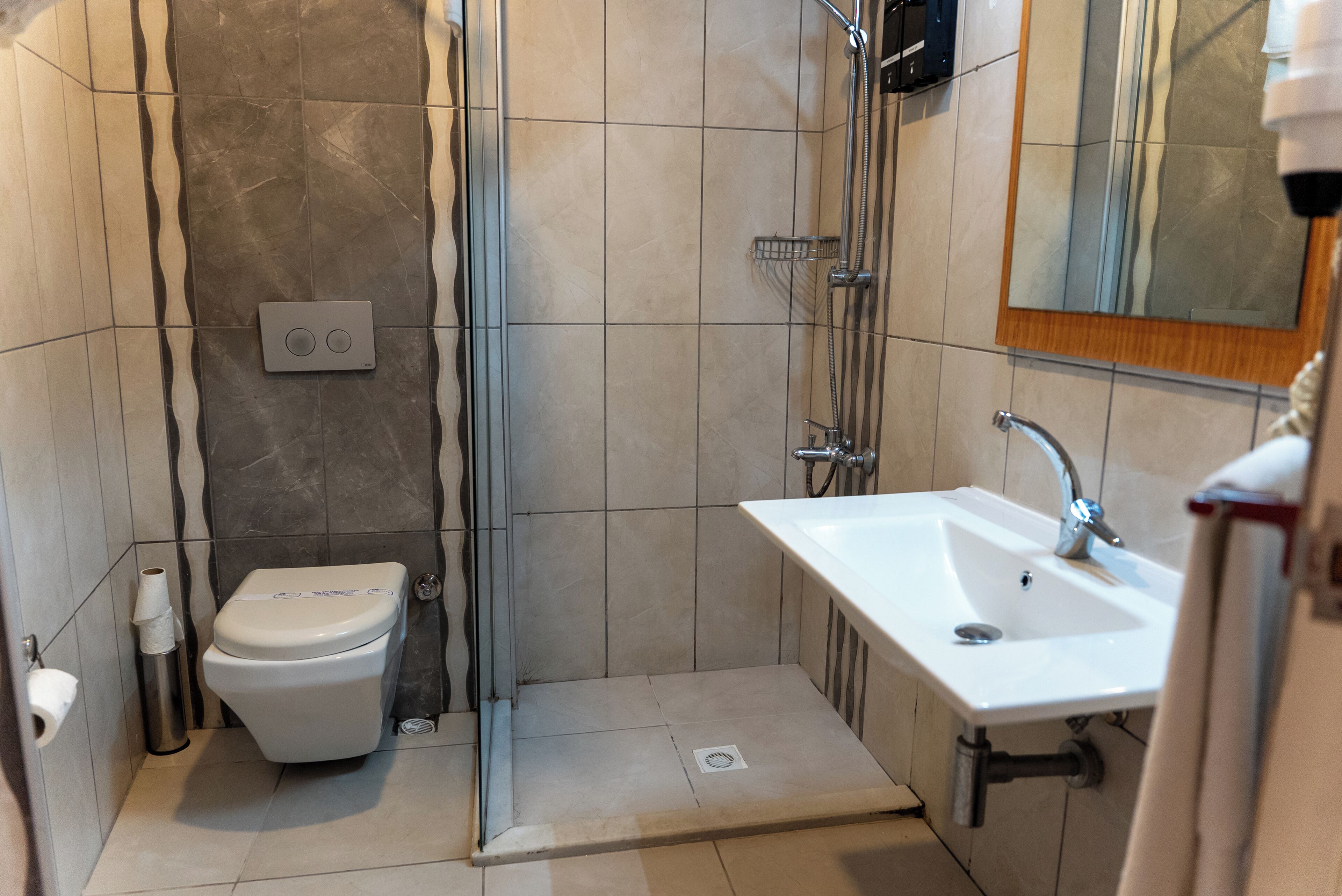 A bathroom with a toilet, shower, sink, and a mirror.