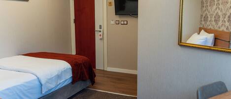 Una habitación de hotel con cama, escritorio, televisión y puerta.