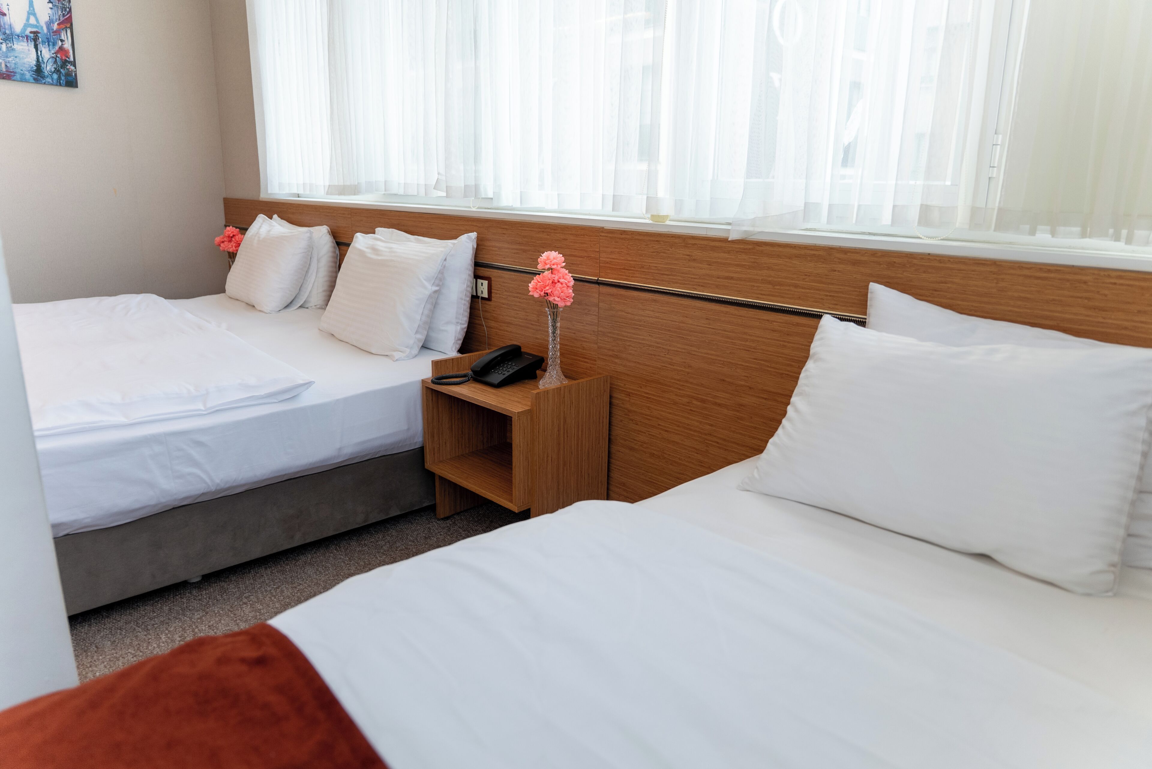 Habitación de hotel con dos camas, cabecera de madera, mesita de noche con teléfono y un jarrón con flores.
