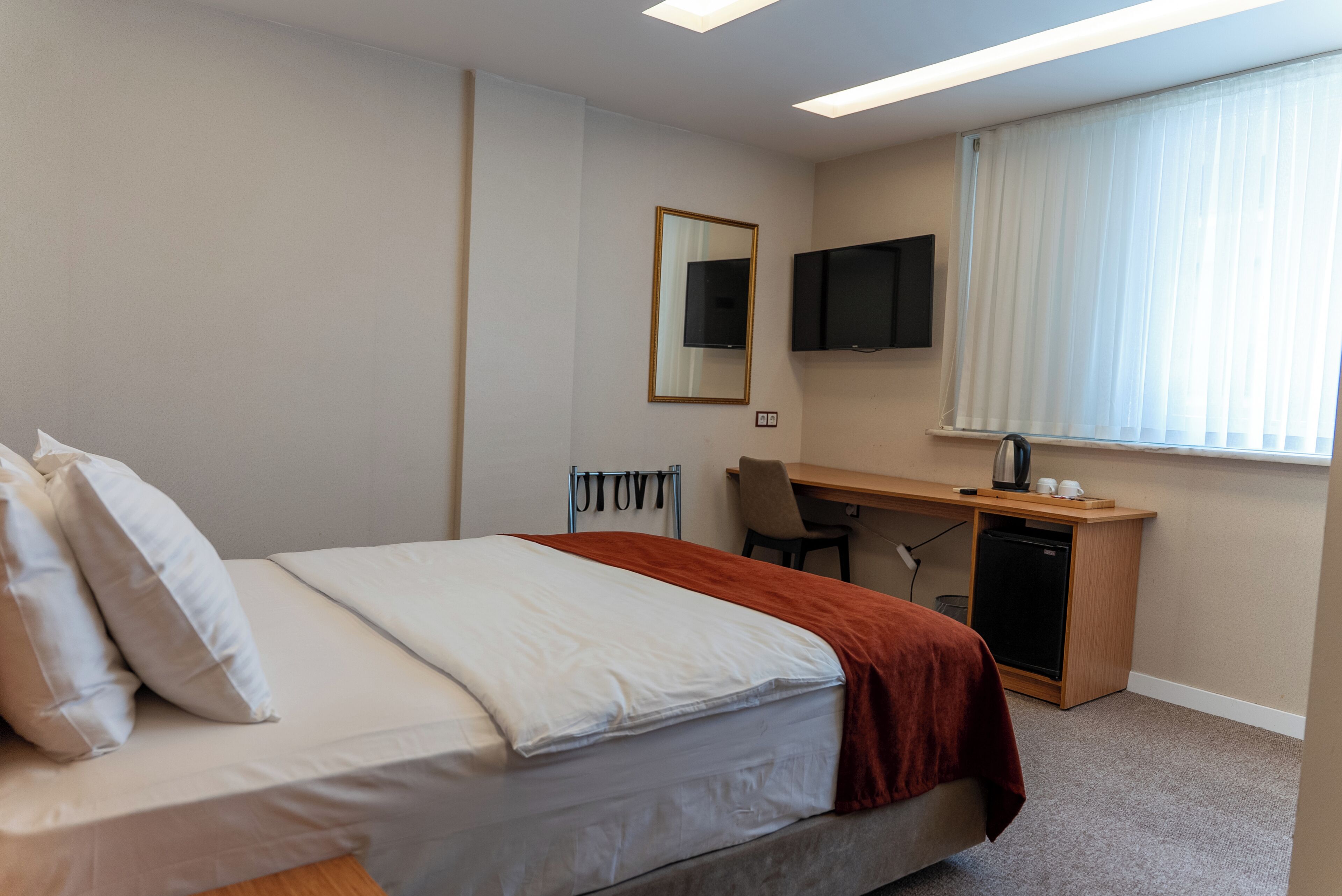 A hotel room with a bed, a desk, a chair, a television, and a window with curtains.