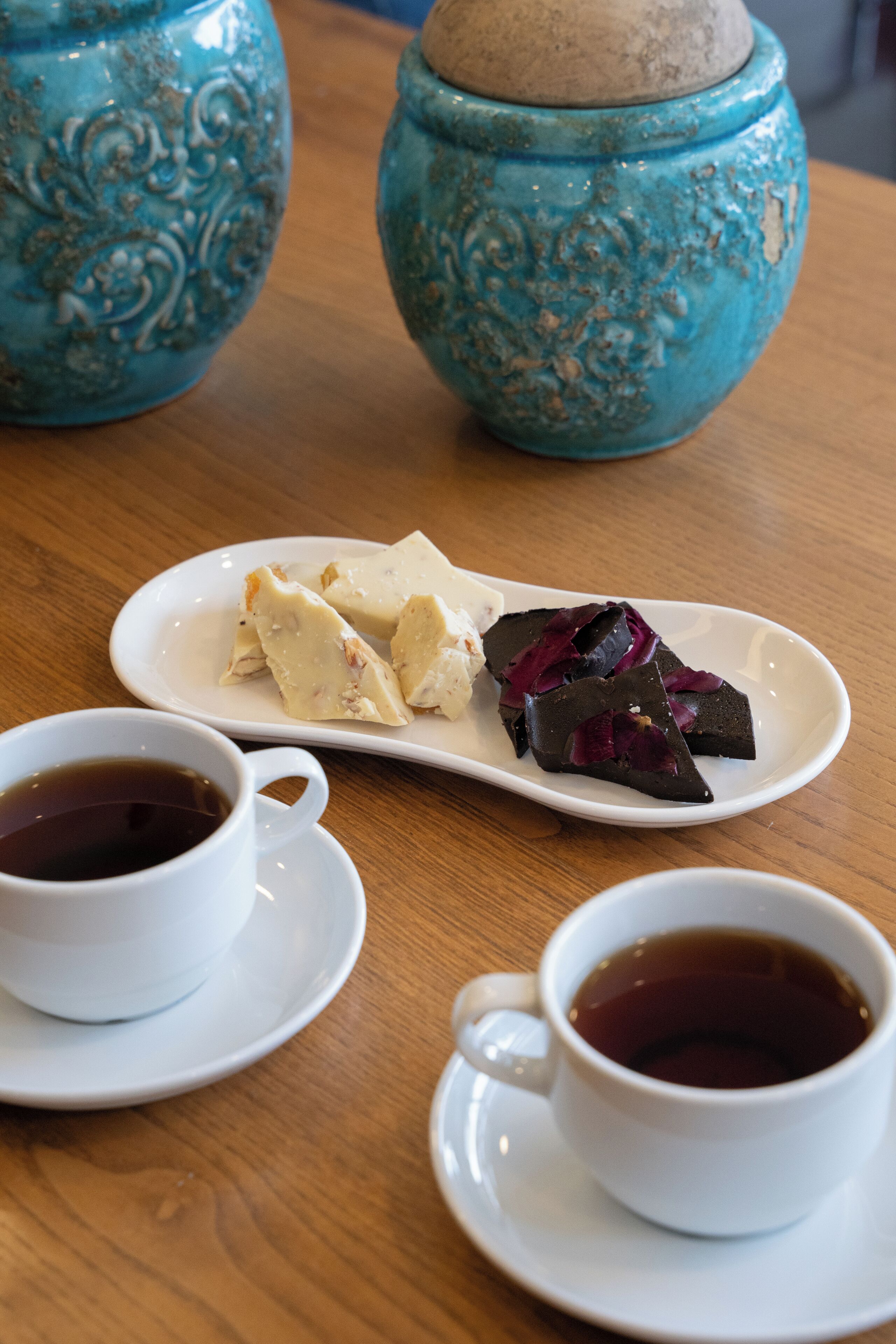 A wooden table with two white cups of tea and a white plate with food.