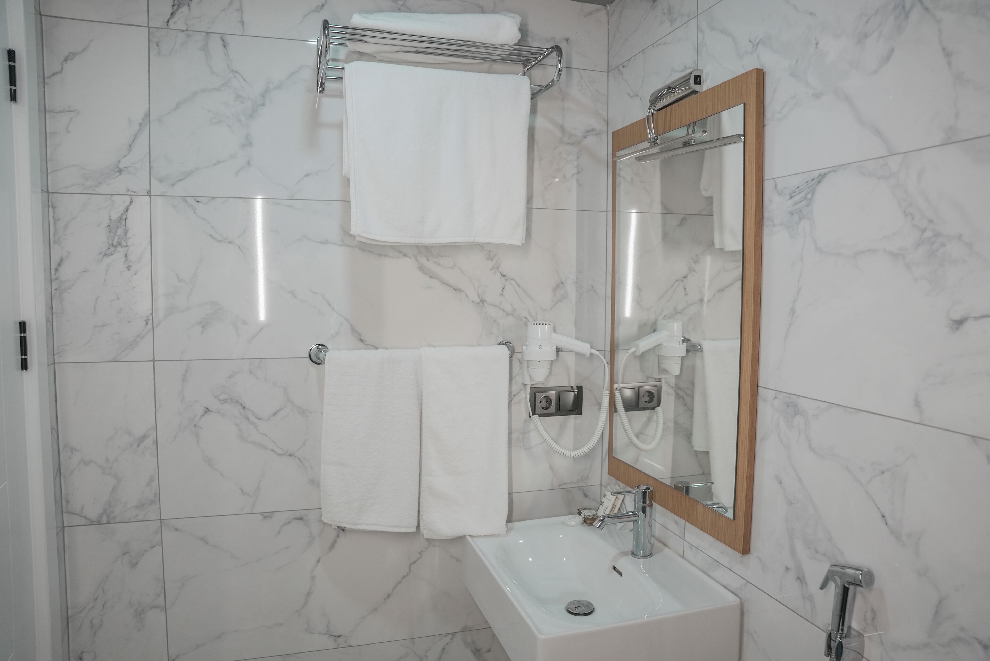 Une salle de bain avec un sol en marbre, un lavabo blanc, un miroir avec un cadre en bois et deux serviettes suspendues à des crochets.