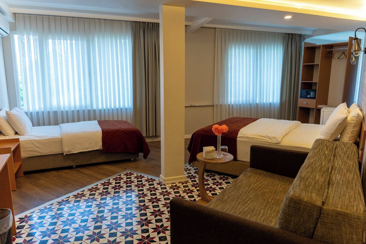 A hotel room with two beds, a sofa, a small table with a vase, and a patterned rug.