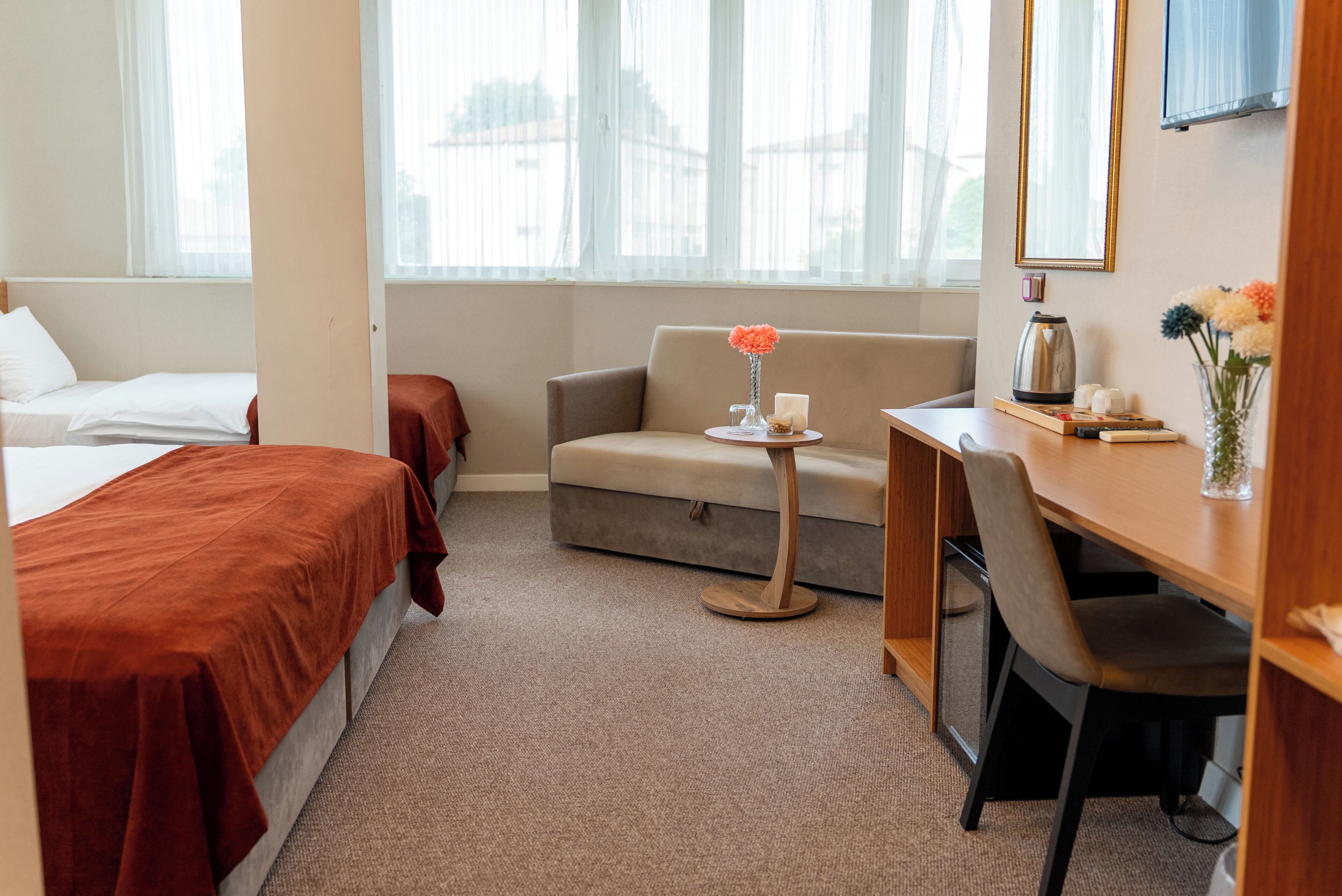Habitación de hotel con cama, sofá, escritorio y una pequeña mesa con un florero.