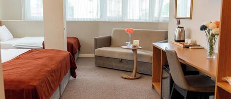 Habitación de hotel con cama, sofá, escritorio y una pequeña mesa con un florero.