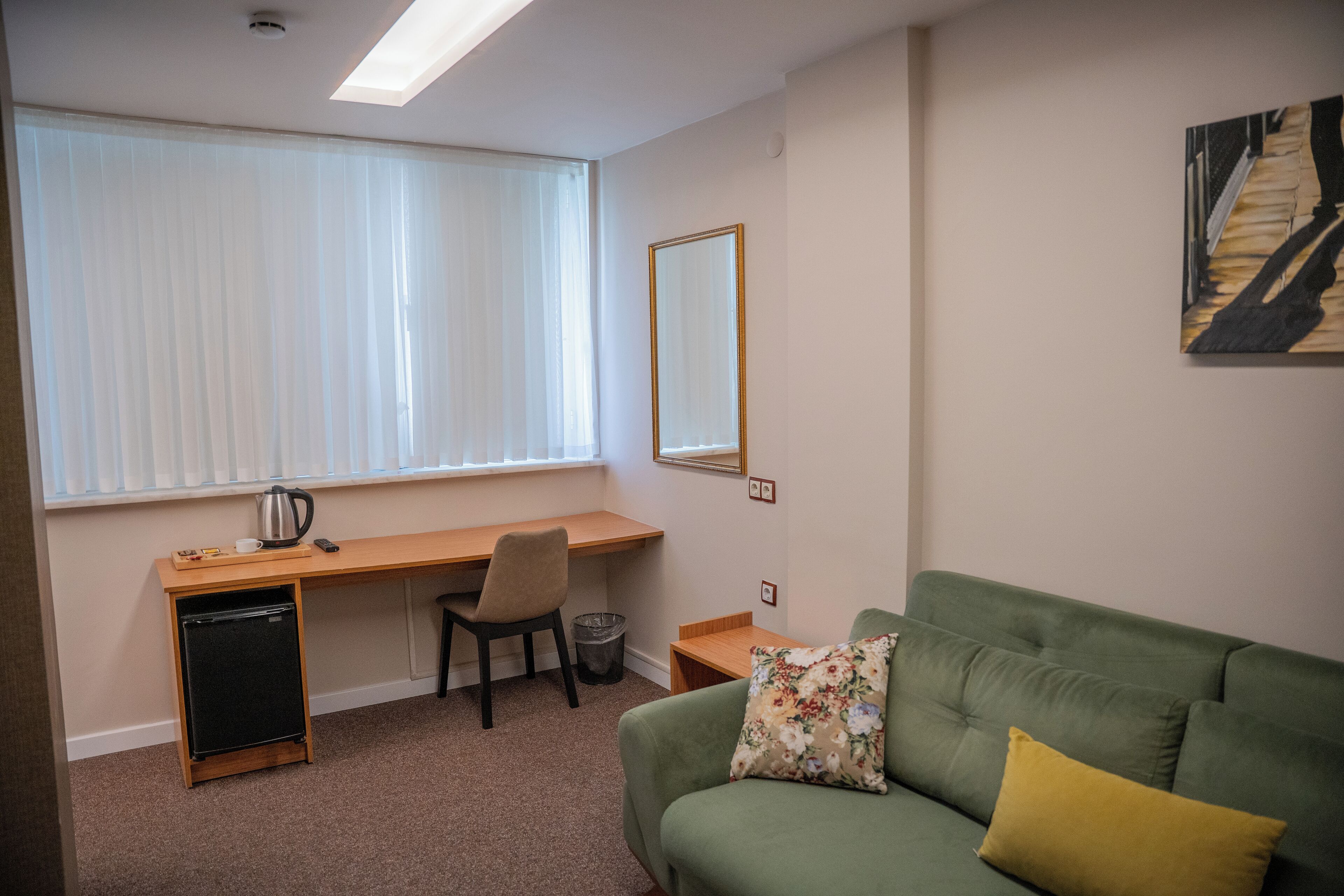 Une pièce comprenant un bureau, une chaise et un canapé vert avec un coussin jaune.