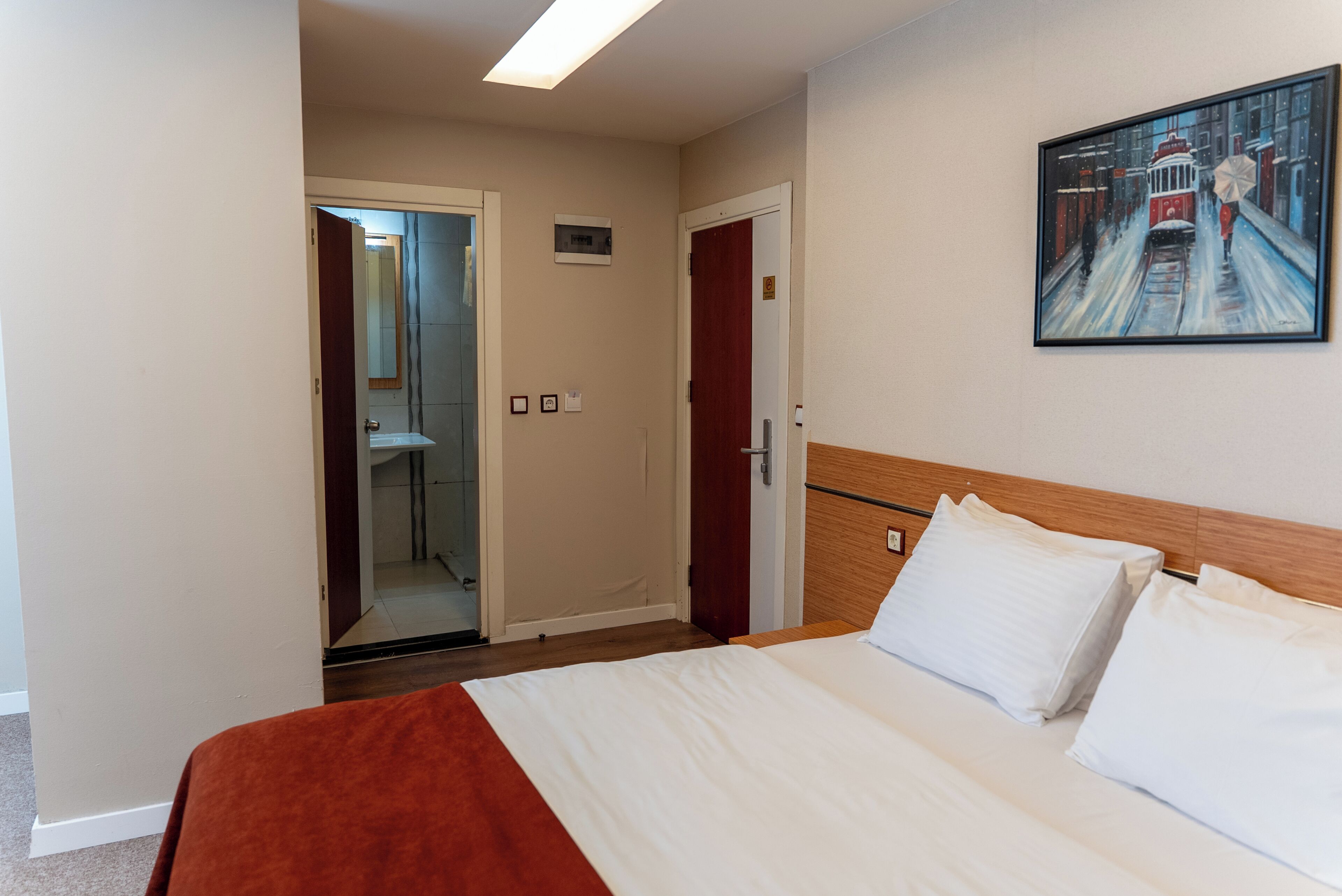 A hotel room with a bed, a painting on the wall, and a door leading to a bathroom.