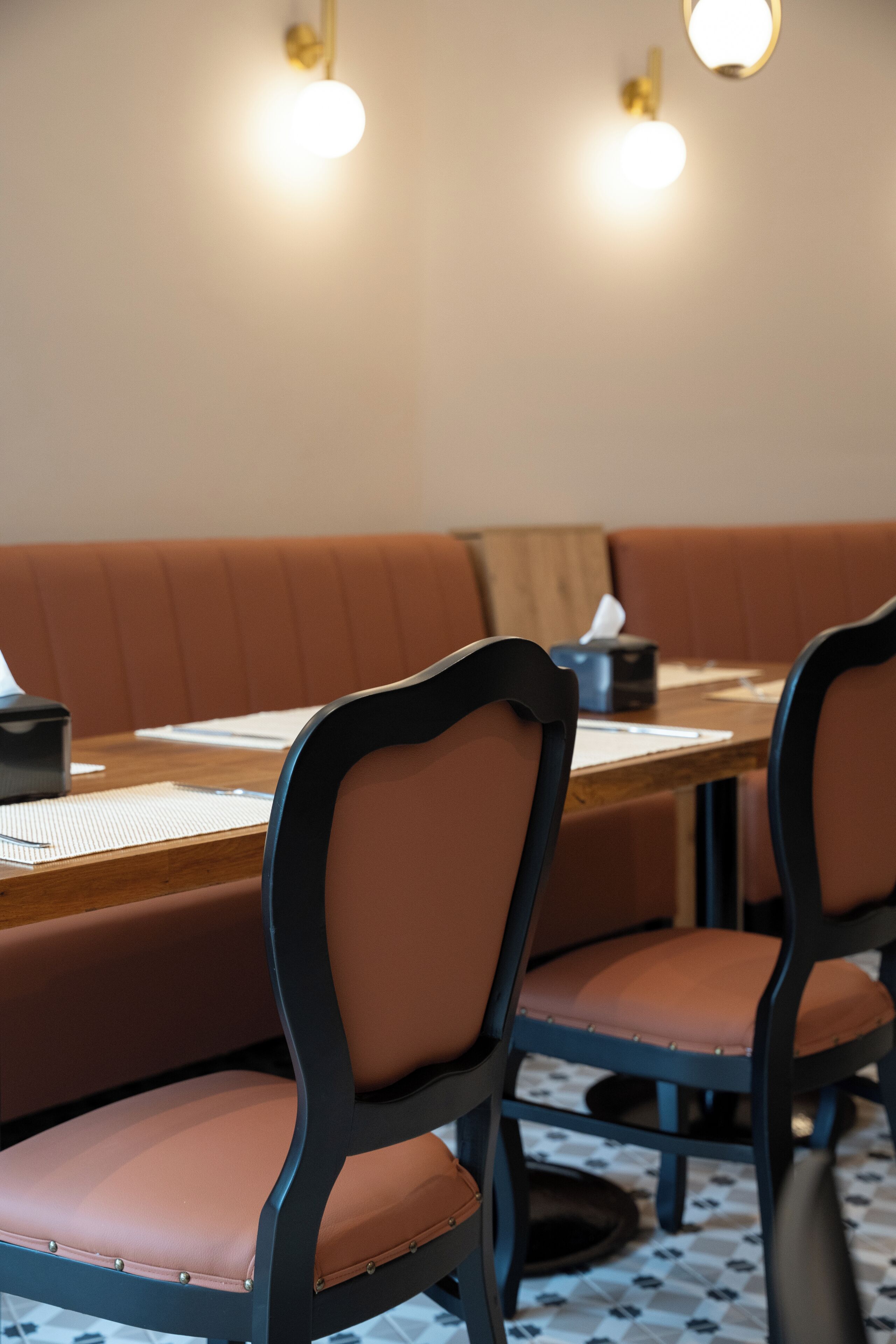 A dining area with a wooden table, cushioned booth seating, and two chairs with dark frames and light-colored cushions.