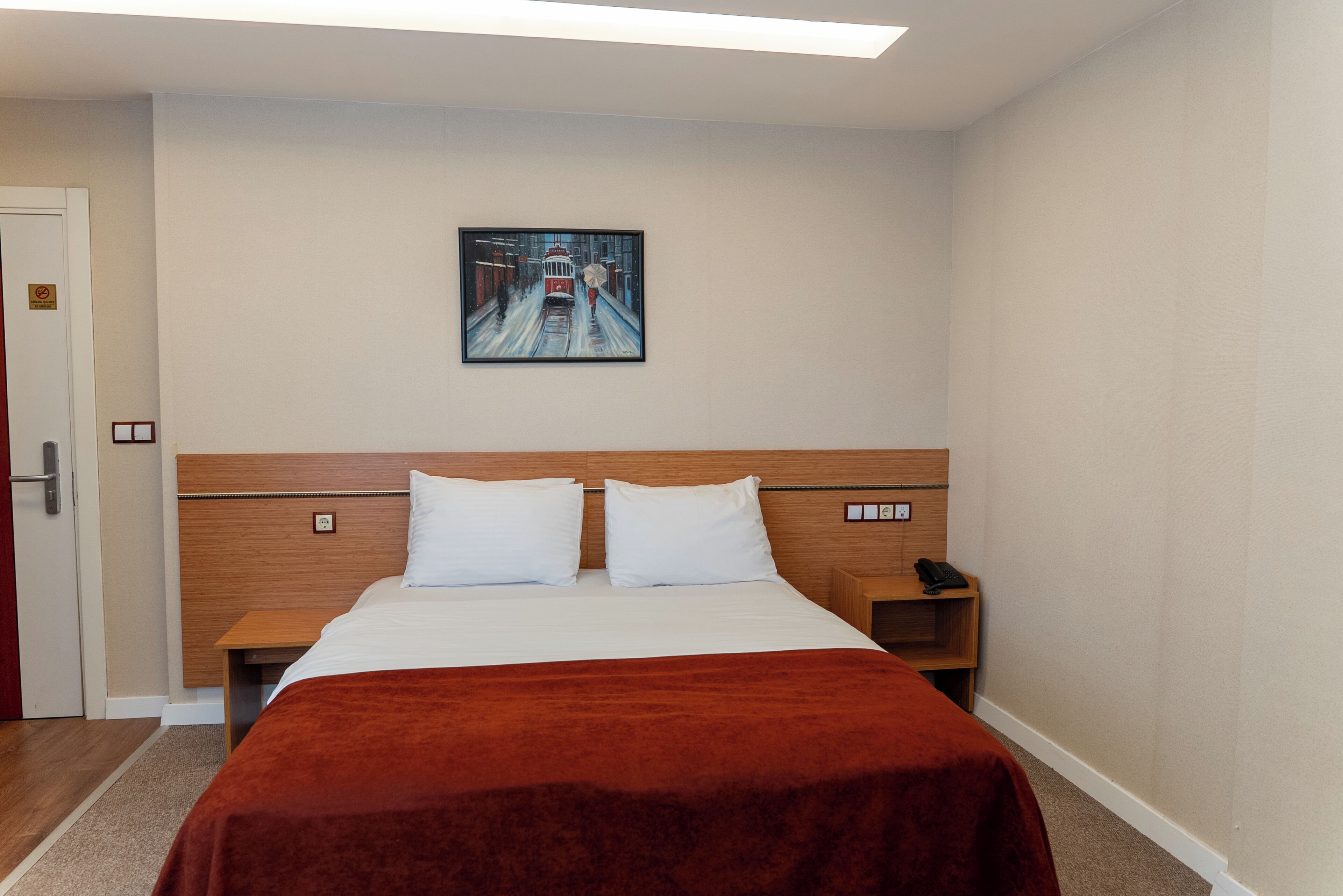 A hotel room with a bed, a nightstand, a painting on the wall, and a door.