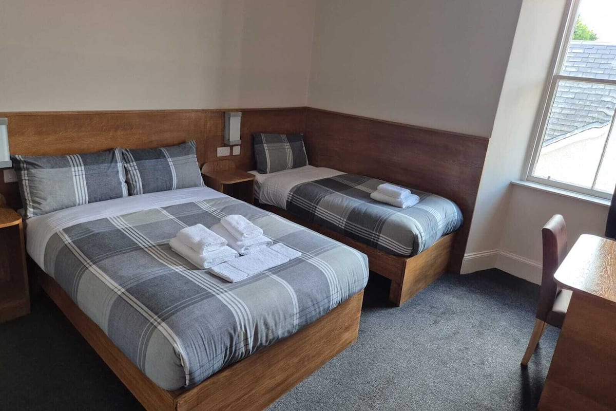 A hotel room with two beds, each with a wooden headboard, grey and white checkered bedding, and neatly folded towels.