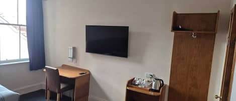 A hotel room with a bed, a desk, a television, a wardrobe, and a small shelf with toiletries.