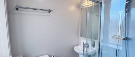 Un baño moderno con inodoro, lavamanos y ducha con mampara de vidrio.