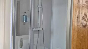 Um chuveiro com divisória de vidro, um chuveiro manual e uma torneira fixada na parede.