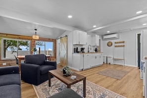 A modern living room with a sofa, a coffee table, and a view of the sea through large windows. - New! Lake Front|PrivateDock|Kayaks&Paddleboards! (Chilton)