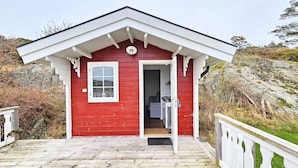 A small red cabin with a white door and window, a wooden deck, and a white railing.