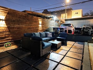 An outdoor seating area with a sofa and chairs, a wooden wall, and a car parked in the background. - Modern 2BR, 2.5BA home in the heart of NoMa/Trinidad (Washington)