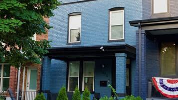 A two-story building with a blue exterior, a porch with a black railing, and a flag on the right side.
