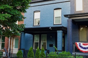 A two-story building with a blue exterior, a porch with a black railing, and a flag on the right side. - Modern 2BR, 2.5BA home in the heart of NoMa/Trinidad (Washington)