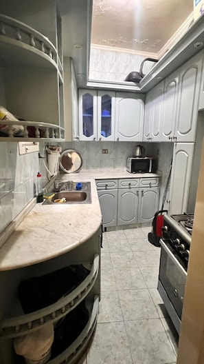 Una cocina compacta con armarios blancos, un microondas, una estufa y un lavabo.