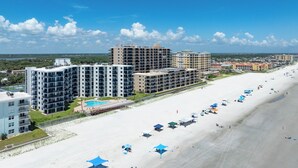 A beachfront hotel with multiple buildings, a swimming pool, and beach umbrellas. - Premier Views, Top Floor Condo, No Drive Beach (New Smyrna Beach)