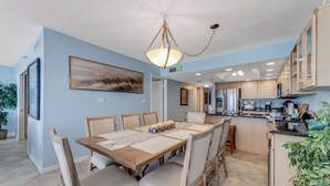 Un coin repas avec une table et des chaises en bois, un luminaire suspendu et une cuisine en arrière-plan.
