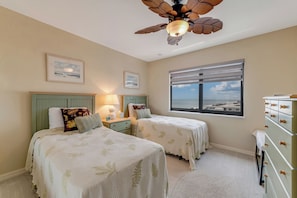 A bedroom with two beds, a ceiling fan, a window with a view, and a dresser. - Premier Views, Top Floor Condo, No Drive Beach (New Smyrna Beach)