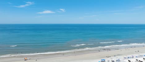 A beach with clear skies, calm waters, and a sandy shore with umbrellas and beach chairs.