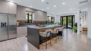 A modern kitchen with a central island, bar stools, and a large window providing natural light. - Modern 4 bedroom stay Oasis Villa with Turkish bath (Coral Gables)
