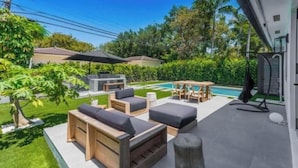 A modern outdoor patio with wooden furniture, a pool, and a well-maintained lawn. - Modern 4 bedroom stay Oasis Villa with Turkish bath (Coral Gables)