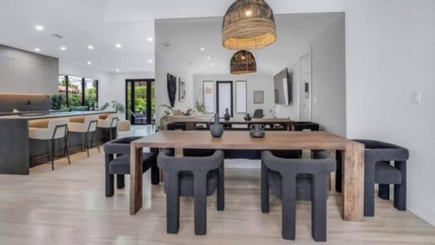 A modern kitchen with a central island, dark chairs, and a hanging light fixture. - Modern 4 bedroom stay Oasis Villa with Turkish bath (Coral Gables)