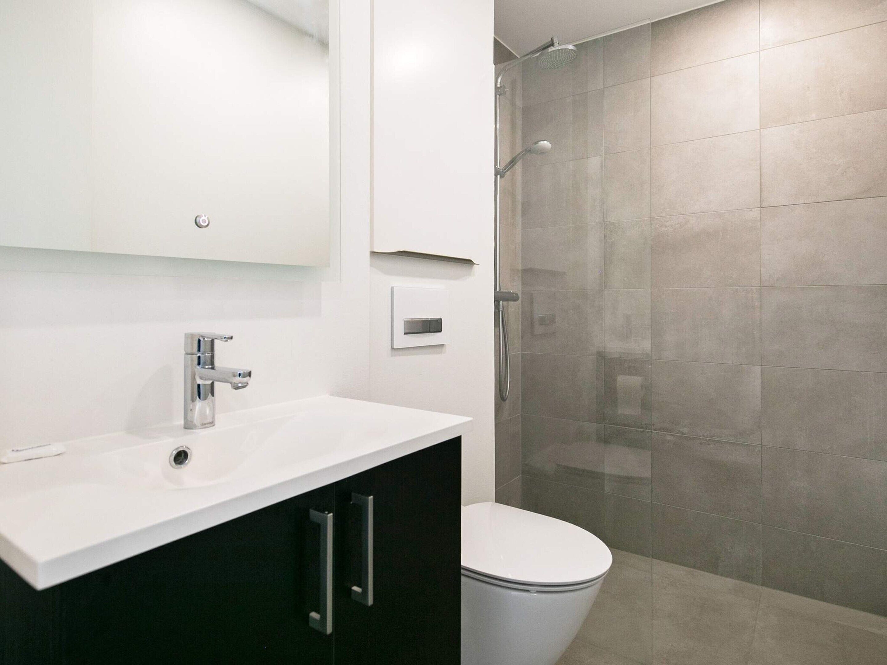 A modern bathroom with a white sink, dark cabinets, a toilet, and a glass-enclosed shower.