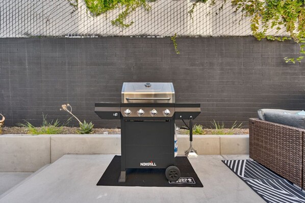 A black outdoor grill with four burners, labeled "NEXGRILL," set on a concrete patio with a black mat.