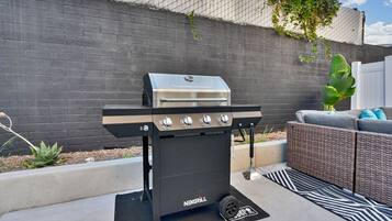A black and silver grill with four burners, positioned on a concrete patio with a black and white patterned rug.