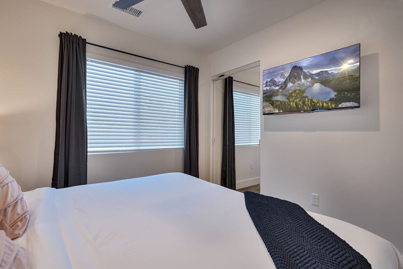 A hotel room with a bed, a painting of a mountain landscape, and a window with blinds.
