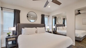 Une chambre d’hôtel avec un grand lit, deux tables de chevet avec des lampes, un ventilateur de plafond et un grand miroir.