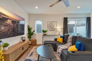 Un salon moderne avec un canapé gris, une table basse ronde et un grand tableau représentant un paysage.