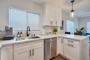 A modern kitchen with white cabinetry, a stainless steel dishwasher, and a coffee machine.