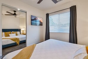 Ein Hotelzimmer mit Bett, Deckenventilator, Fenster mit Vorhängen und einem Gemälde an der Wand.