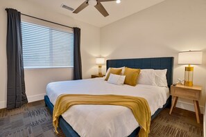 A hotel room with a large bed, two bedside tables, a ceiling fan, and a window with curtains.