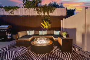 A cozy outdoor seating area with a fire pit, a sectional sofa, and a dining table.